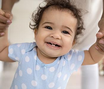 Toddler walking and smiling at camera with aid of adult